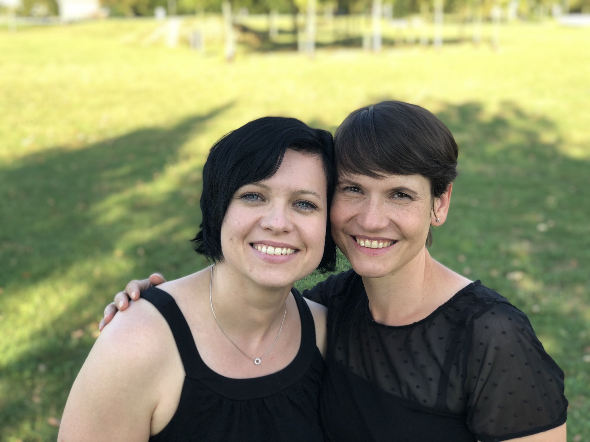 Anika und Melanie lachen Arm in Arm im Park